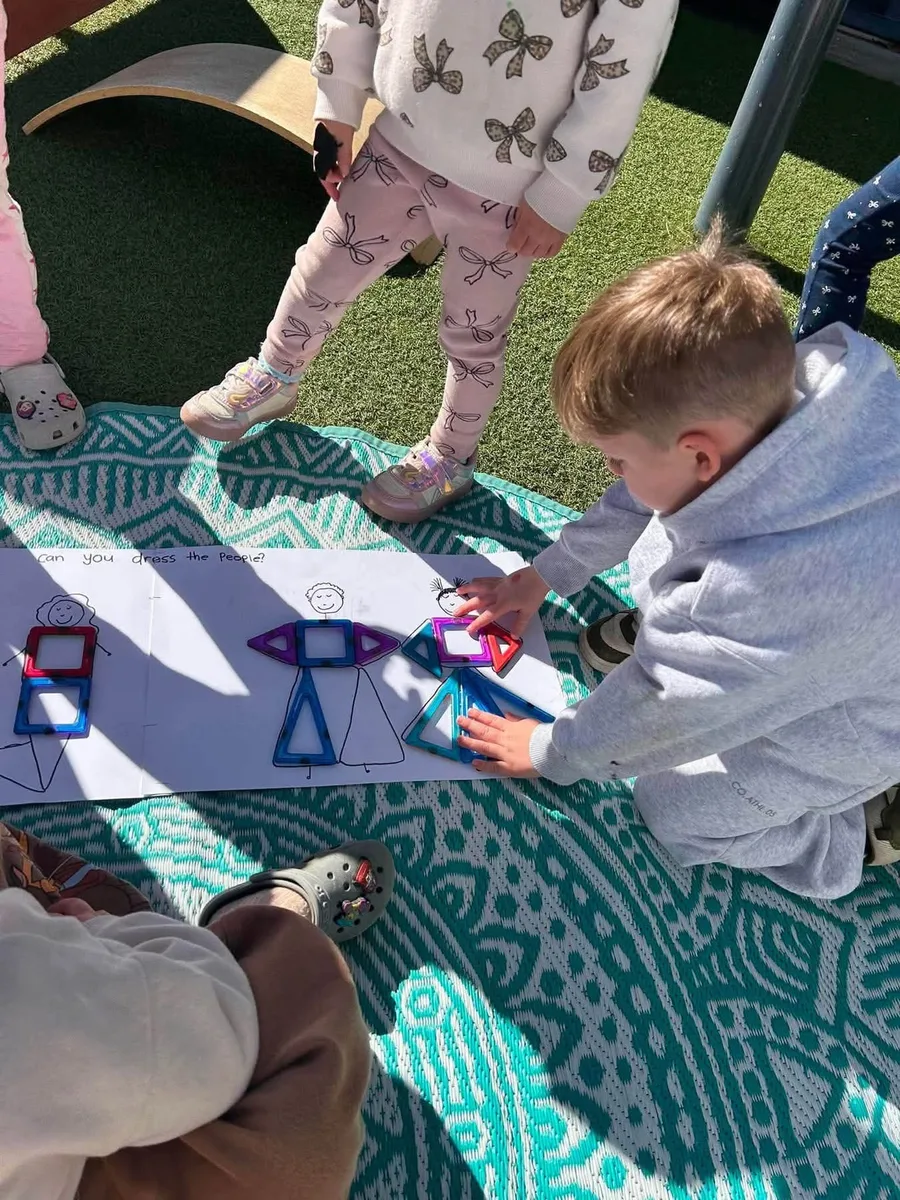 Two tamariki building with magnetic shapes on a patterned mat