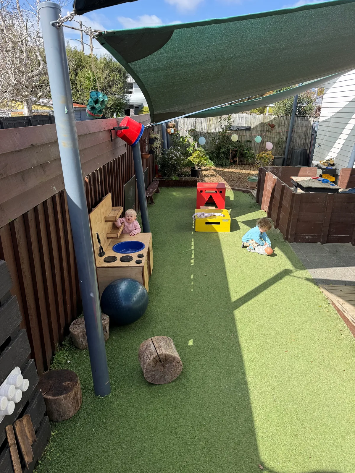A covered outdoor play space with ride-on toys, natural timber and turf