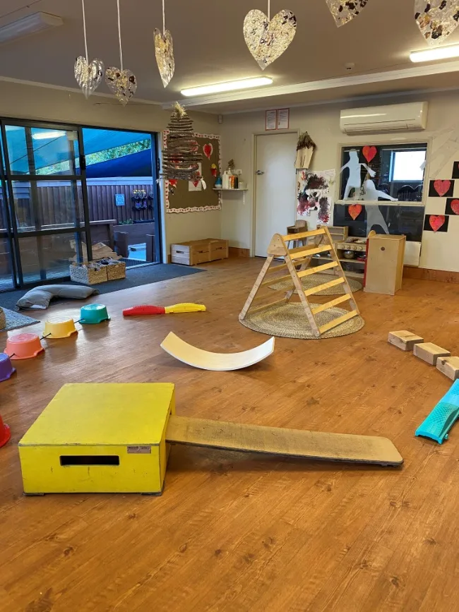 An indoor movement space set up with wooden ramps, blocks and a climbing frame